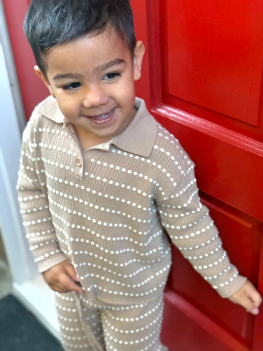 Child wearing an Atelier knit set beside a red door