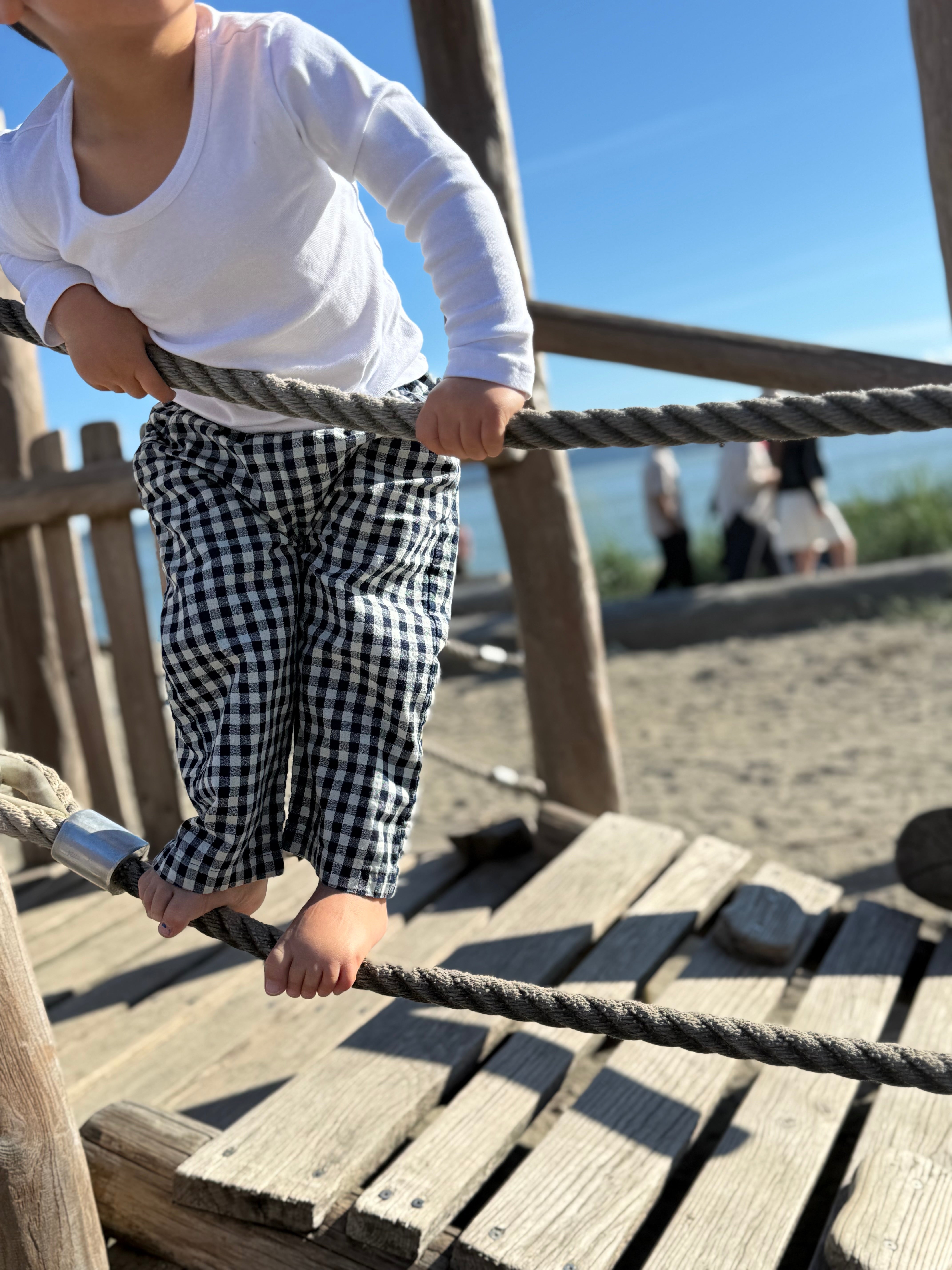 Child on a playground structure with wooden planks and ropes.