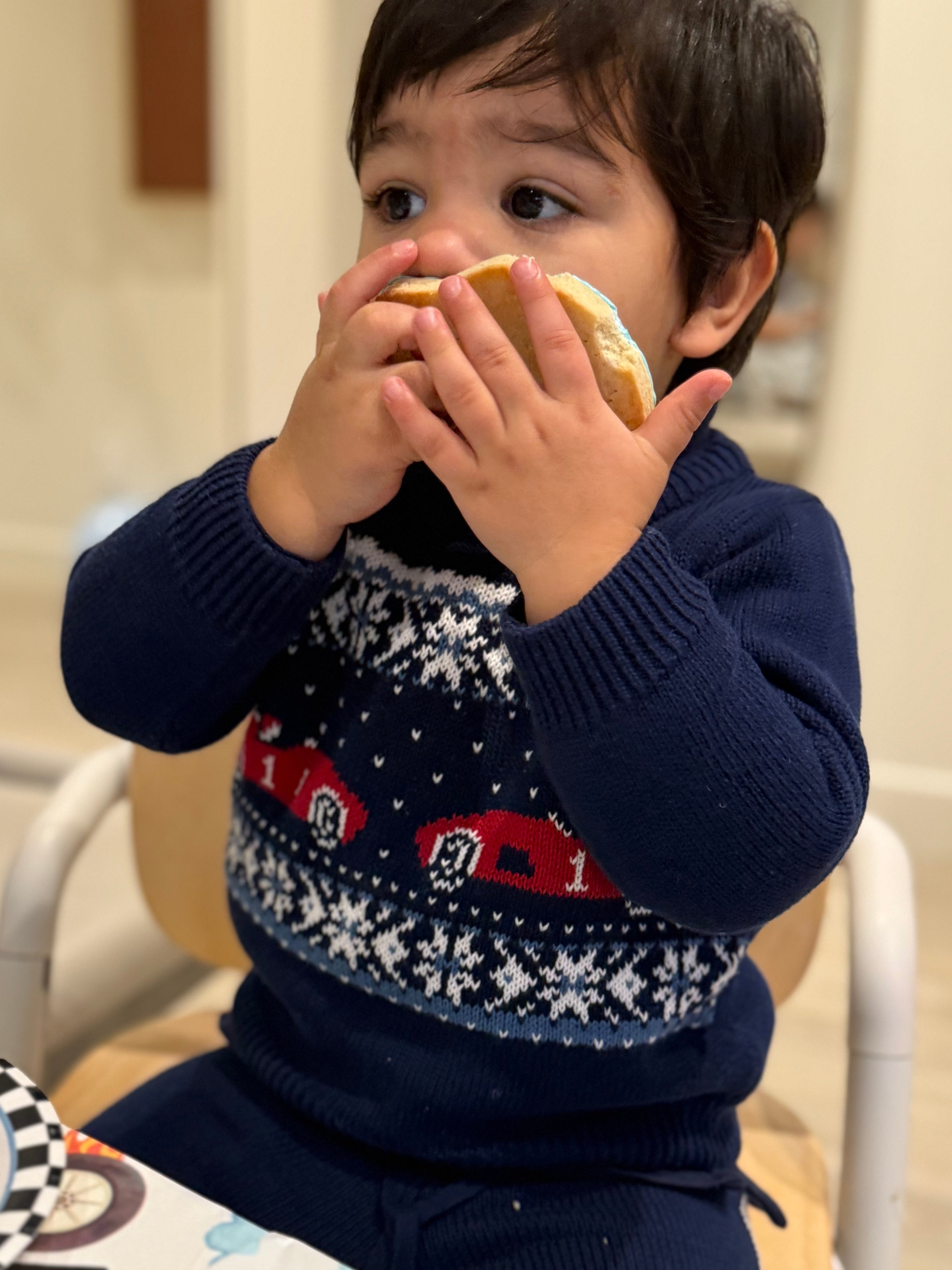 Child wearing a navy sweater with a pattern, eating a piece of food.