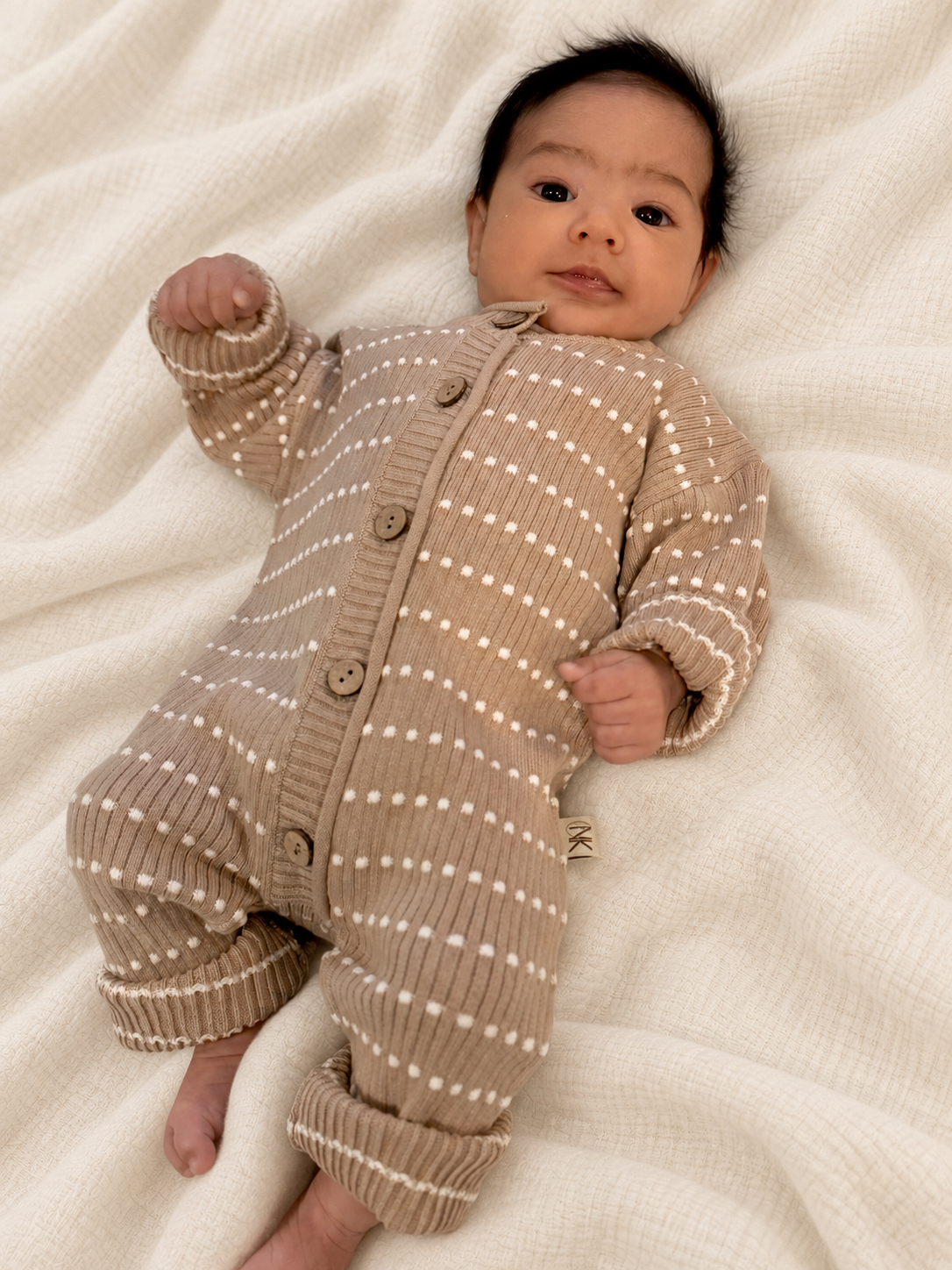 Baby lying on a blanket in a brown-beige Atelier knit romper