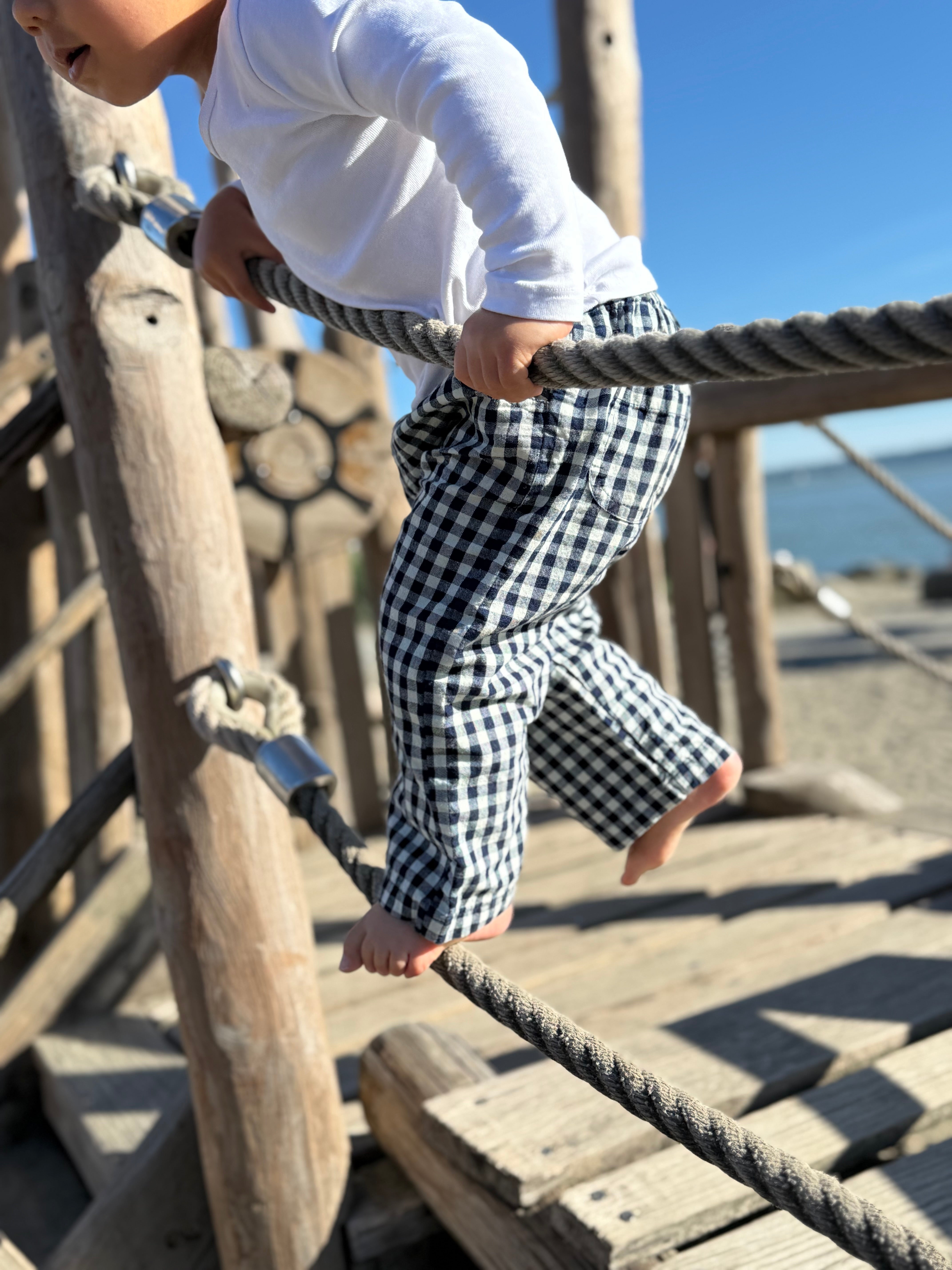 Child climbing on a wooden playground structure with a clear blue sky in the background