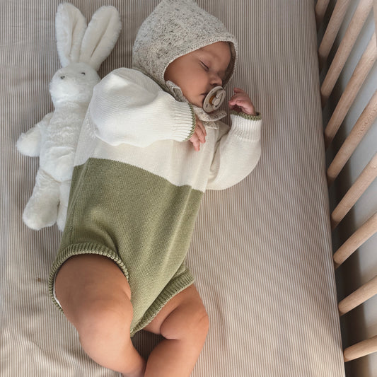 Baby in a green and white outfit lying on a crib with a white rabbit toy.