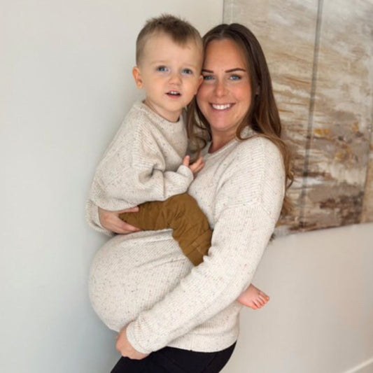 Mother holding her son while pregnant in matching sweaters
