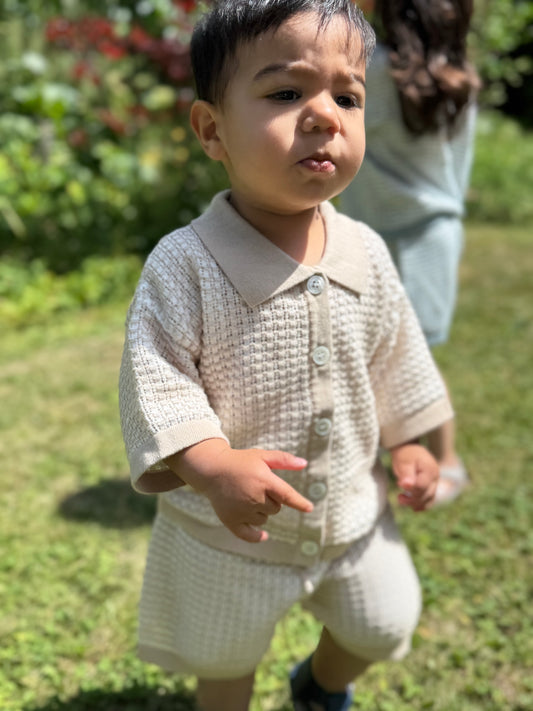 Child in a light-colored outfit standing outdoors on grass