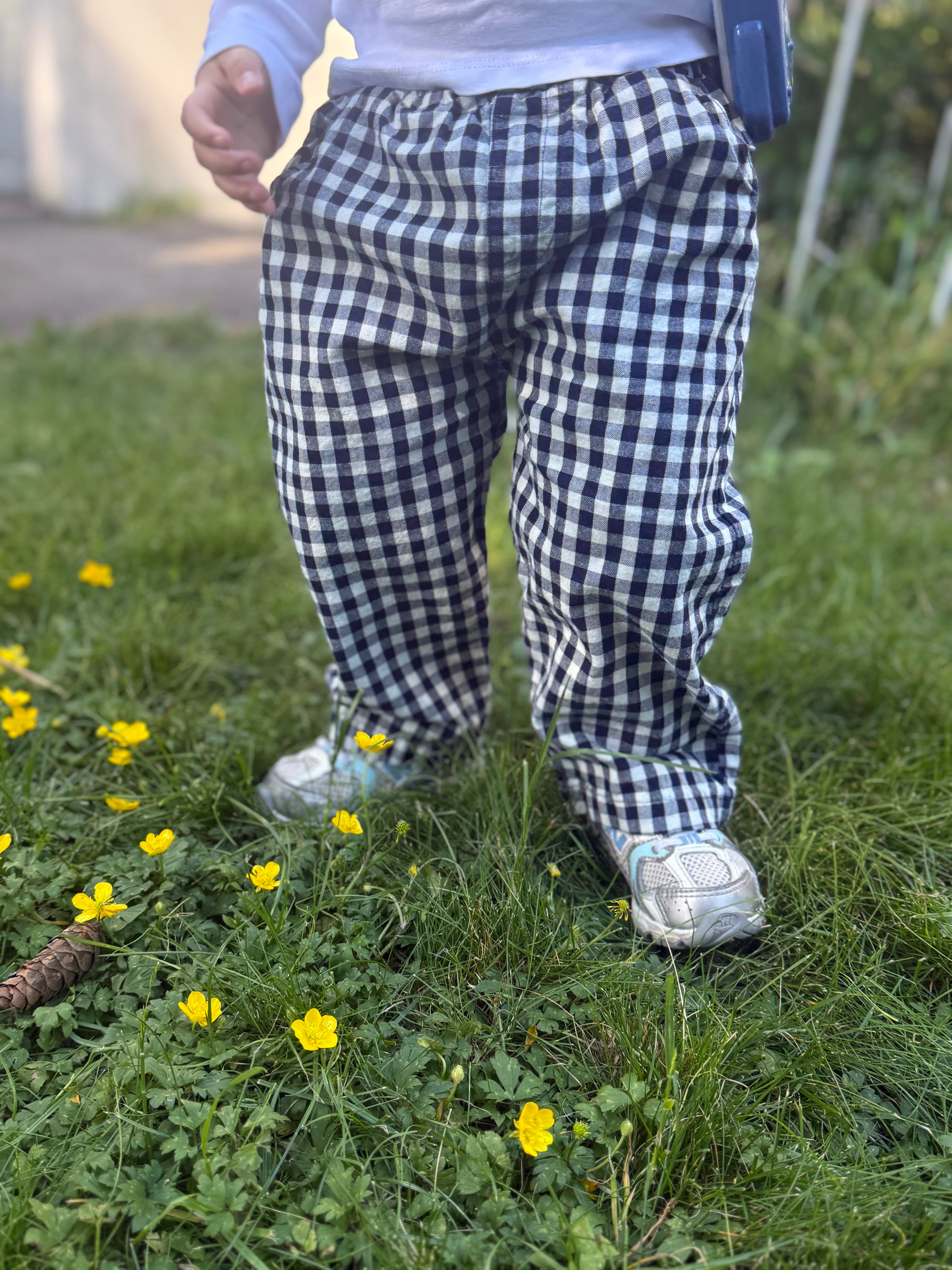 Person wearing blue and white checkered pants standing on grass with yellow flowers.