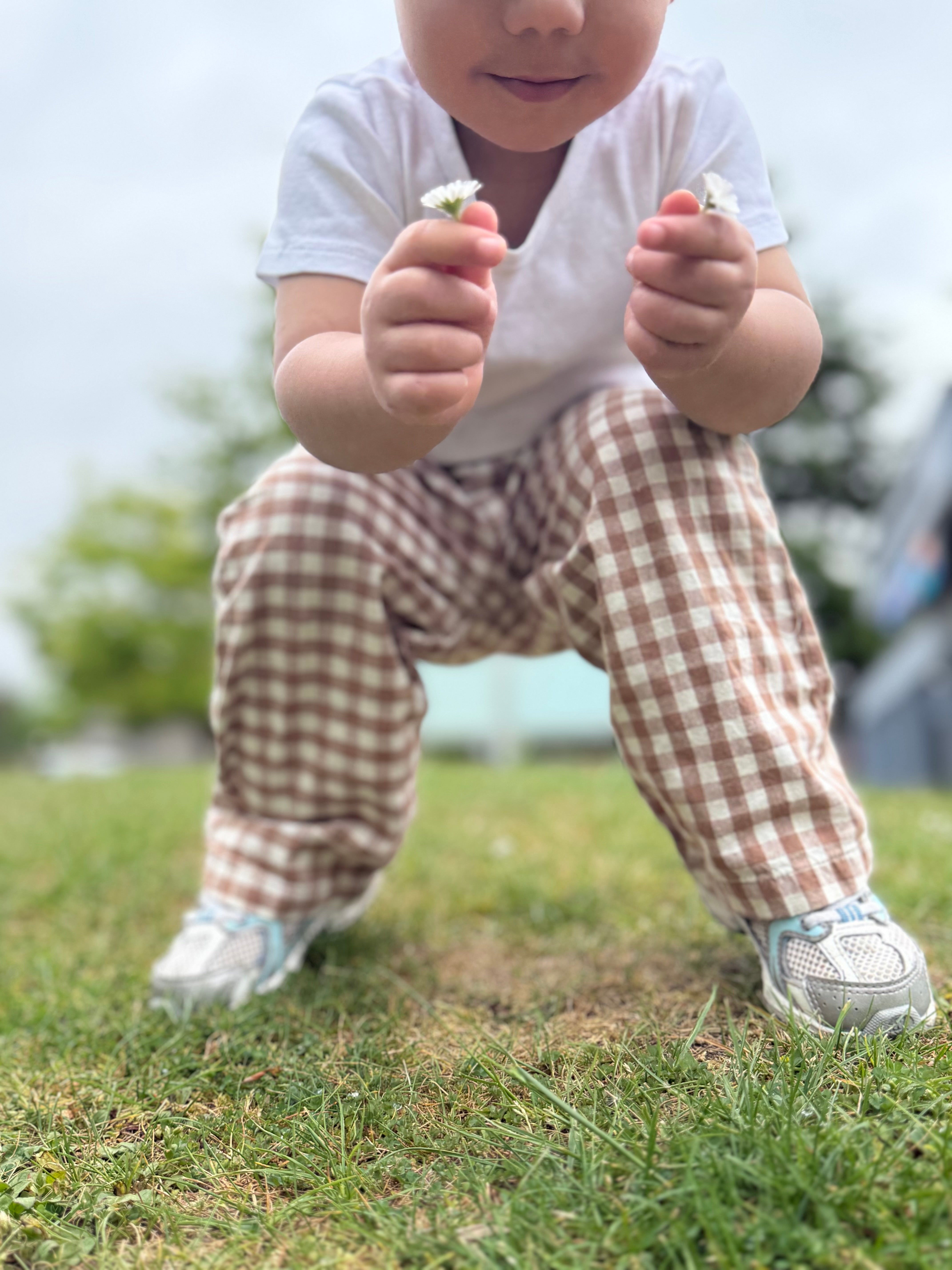 Child in checkered pants and white shirt holding flowers on grass