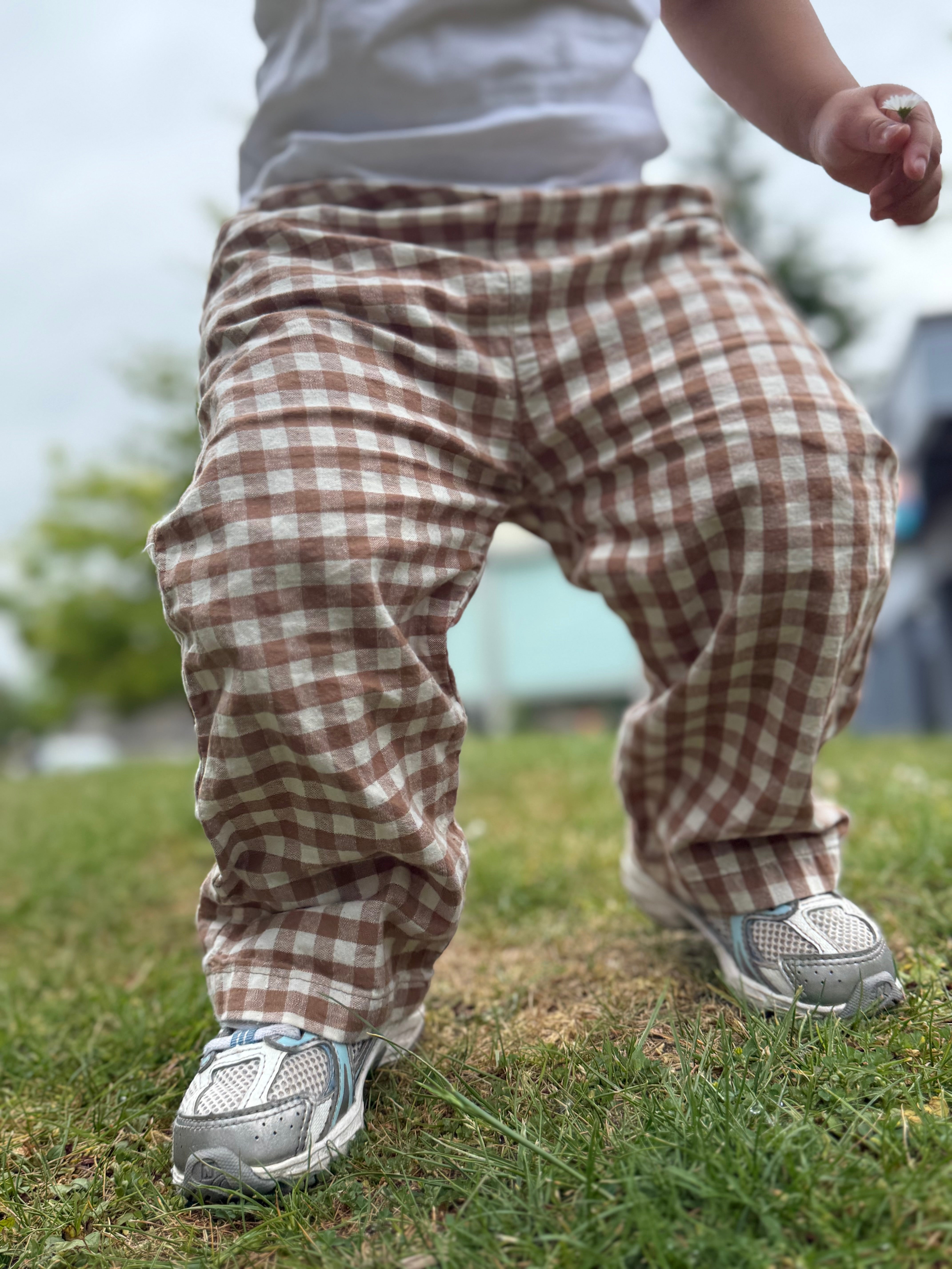 Child wearing brown plaid pants and white sneakers on grass