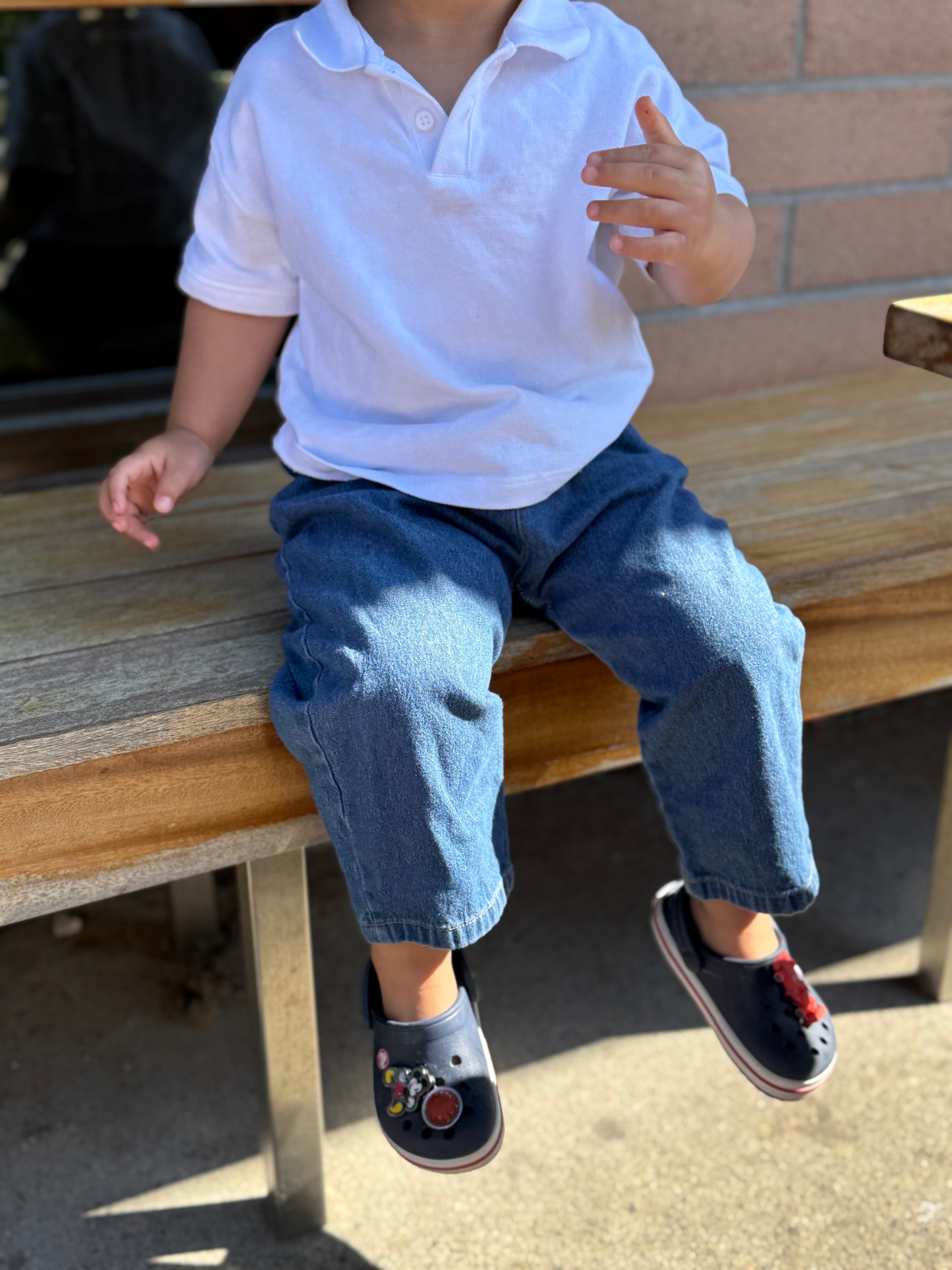 Child sitting on a wooden bench wearing a white shirt and blue jeans.