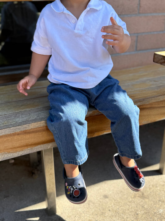 Child sitting on a wooden bench wearing a white shirt and blue jeans.
