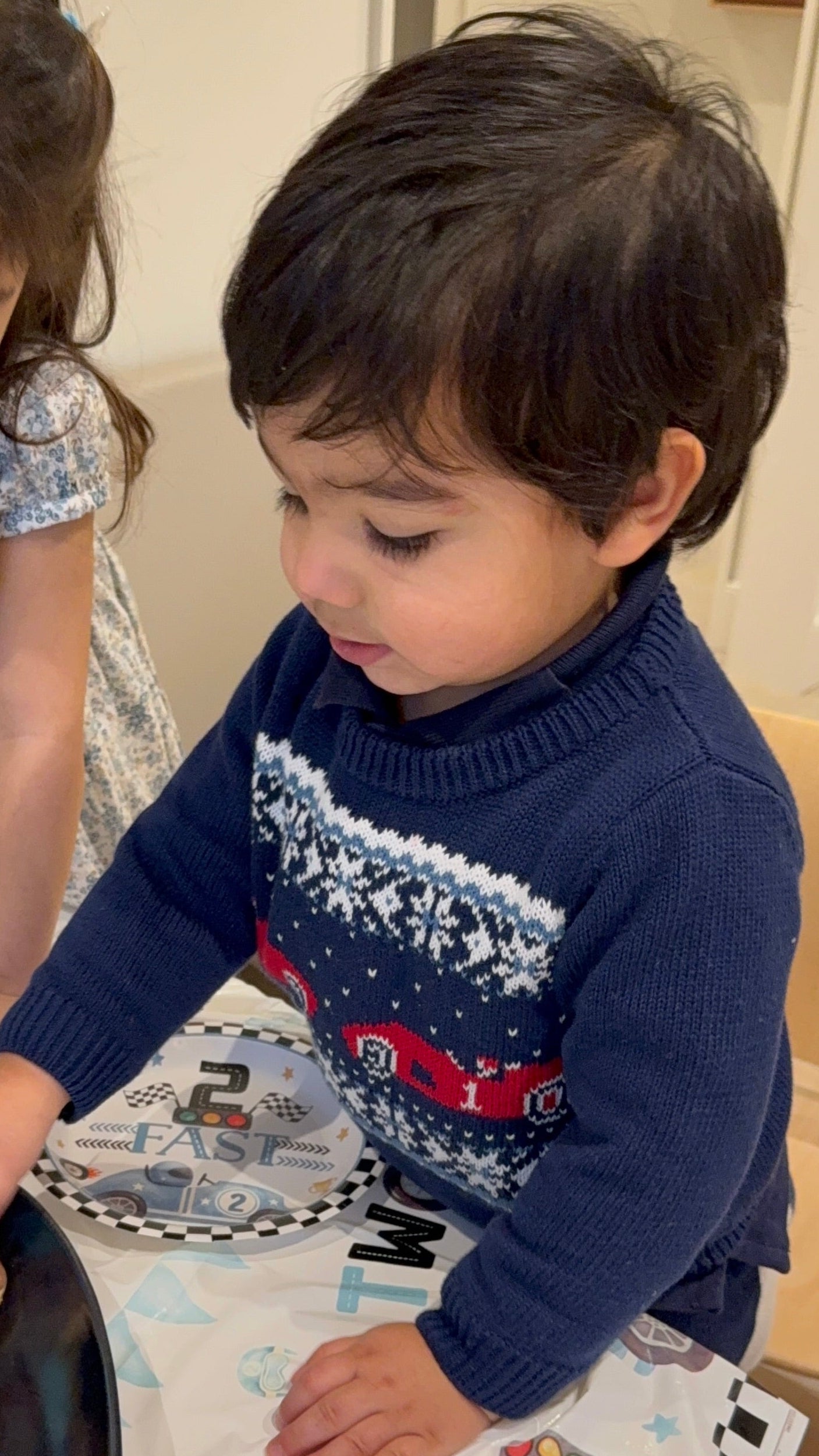 Child wearing a blue sweater with a car design, sitting at a table.