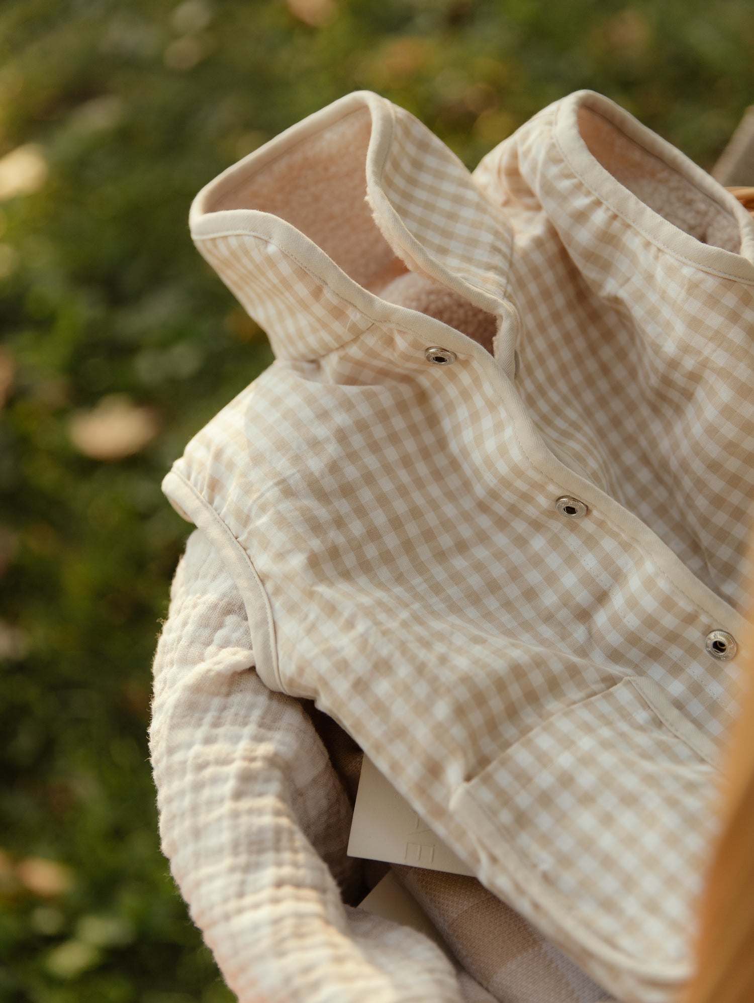 Beige checkered baby vest against a blurred green background