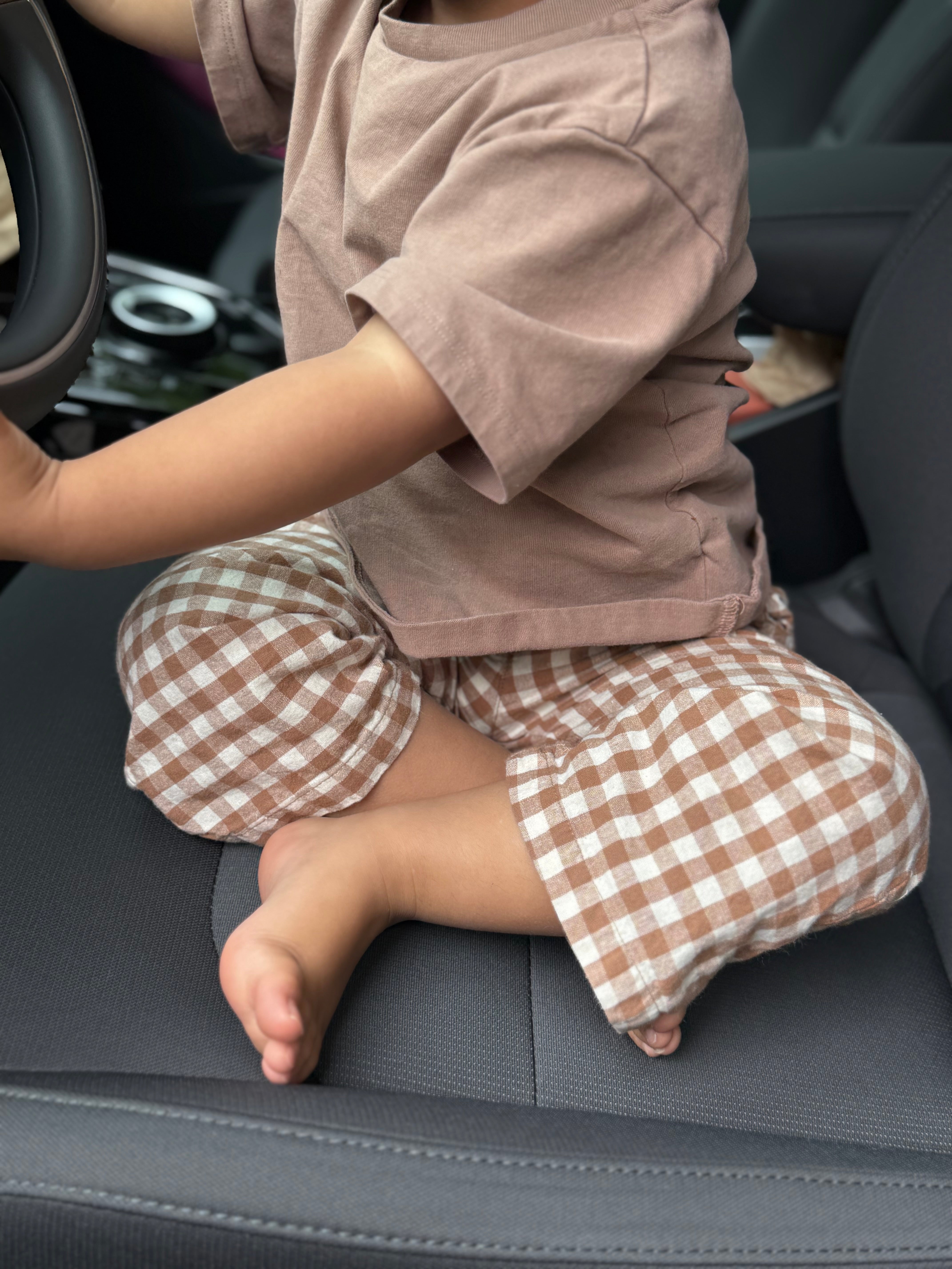 Child sitting in a car seat wearing a brown outfit with gingham pants.