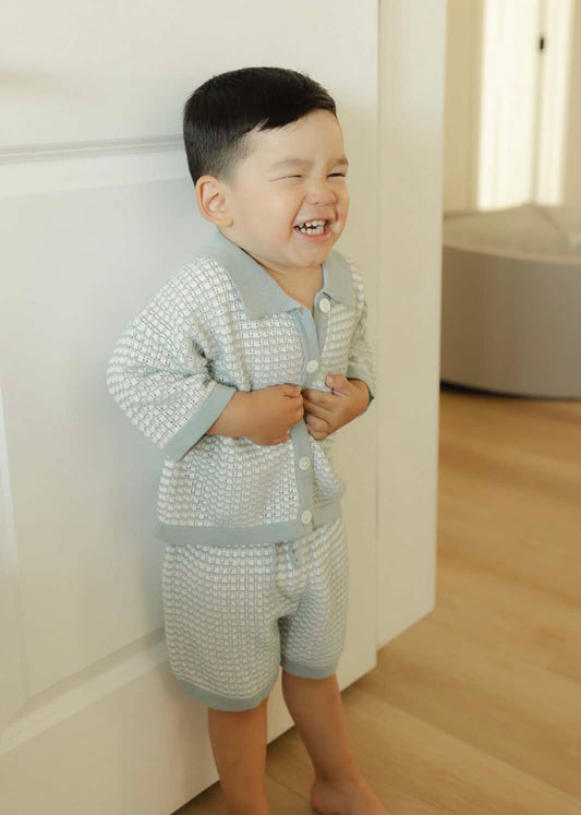 Child wearing a light blue knitted outfit standing indoors with a neutral background