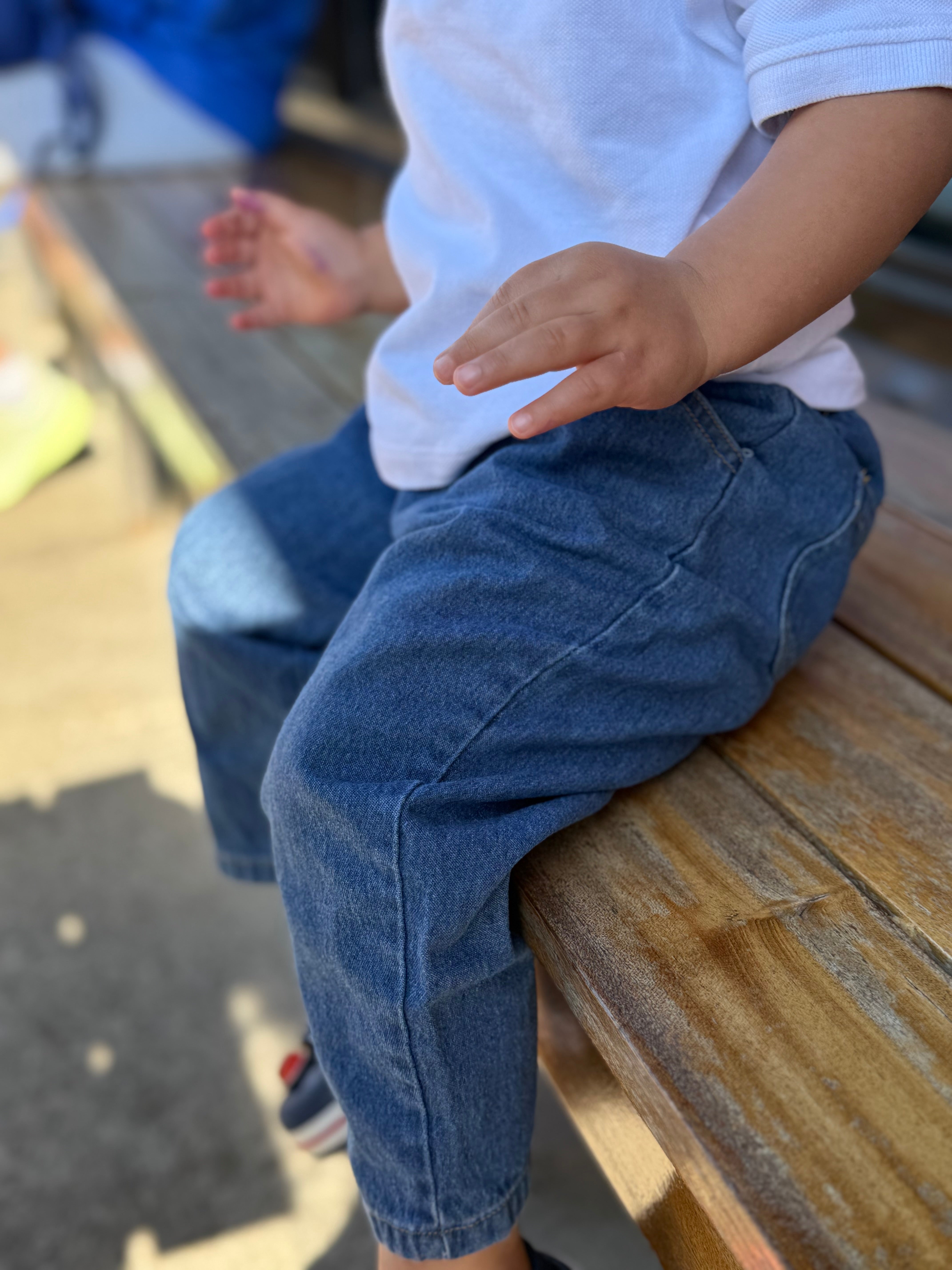Child wearing blue jeans and a white shirt sitting on a wooden surface.