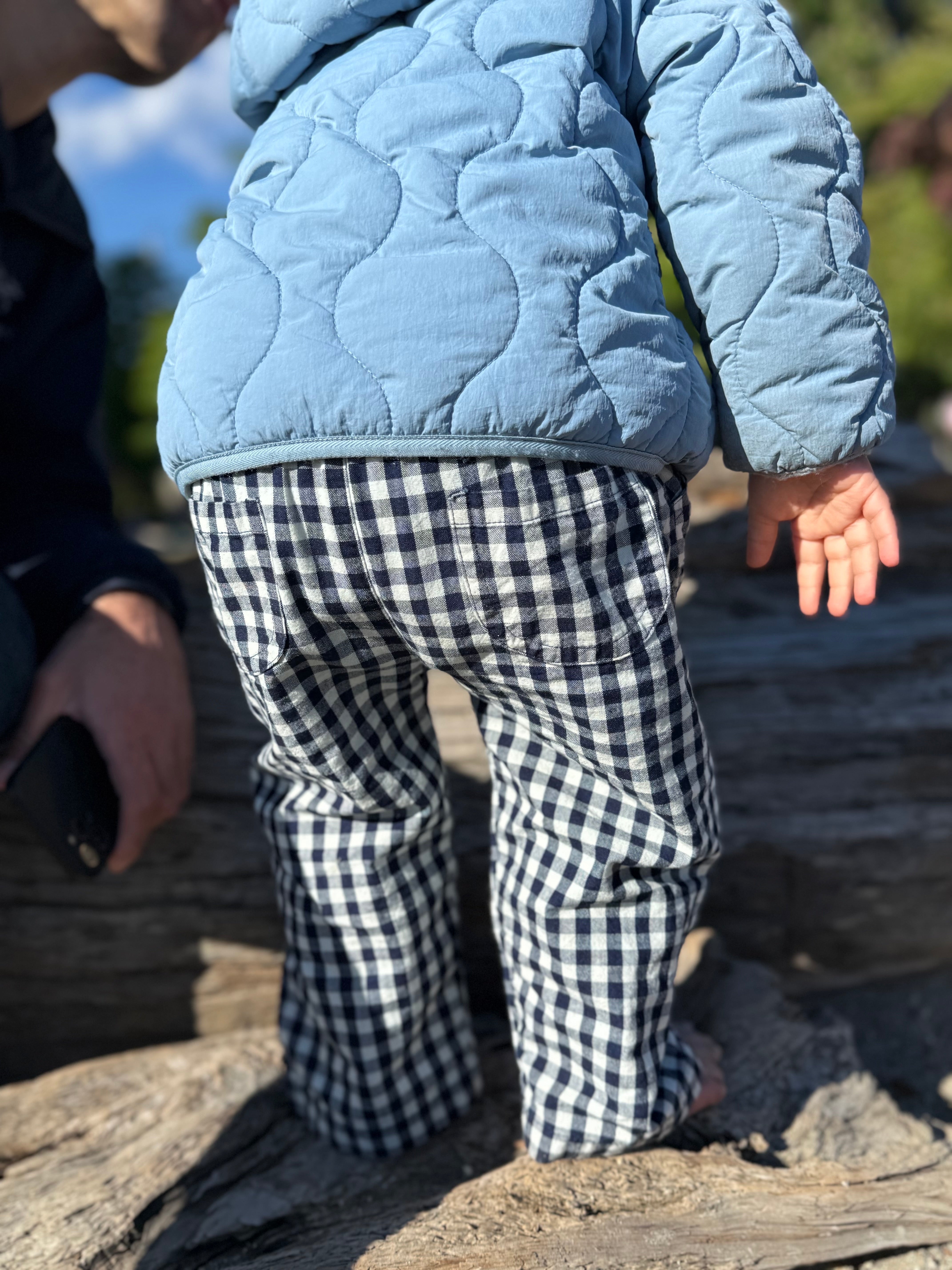 Child wearing a blue quilted jacket and checkered pants standing on rocks outdoors.