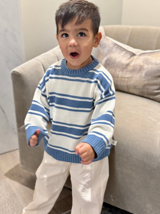 Child standing by a sofa in a blue and cream striped knit sweater and cream pants