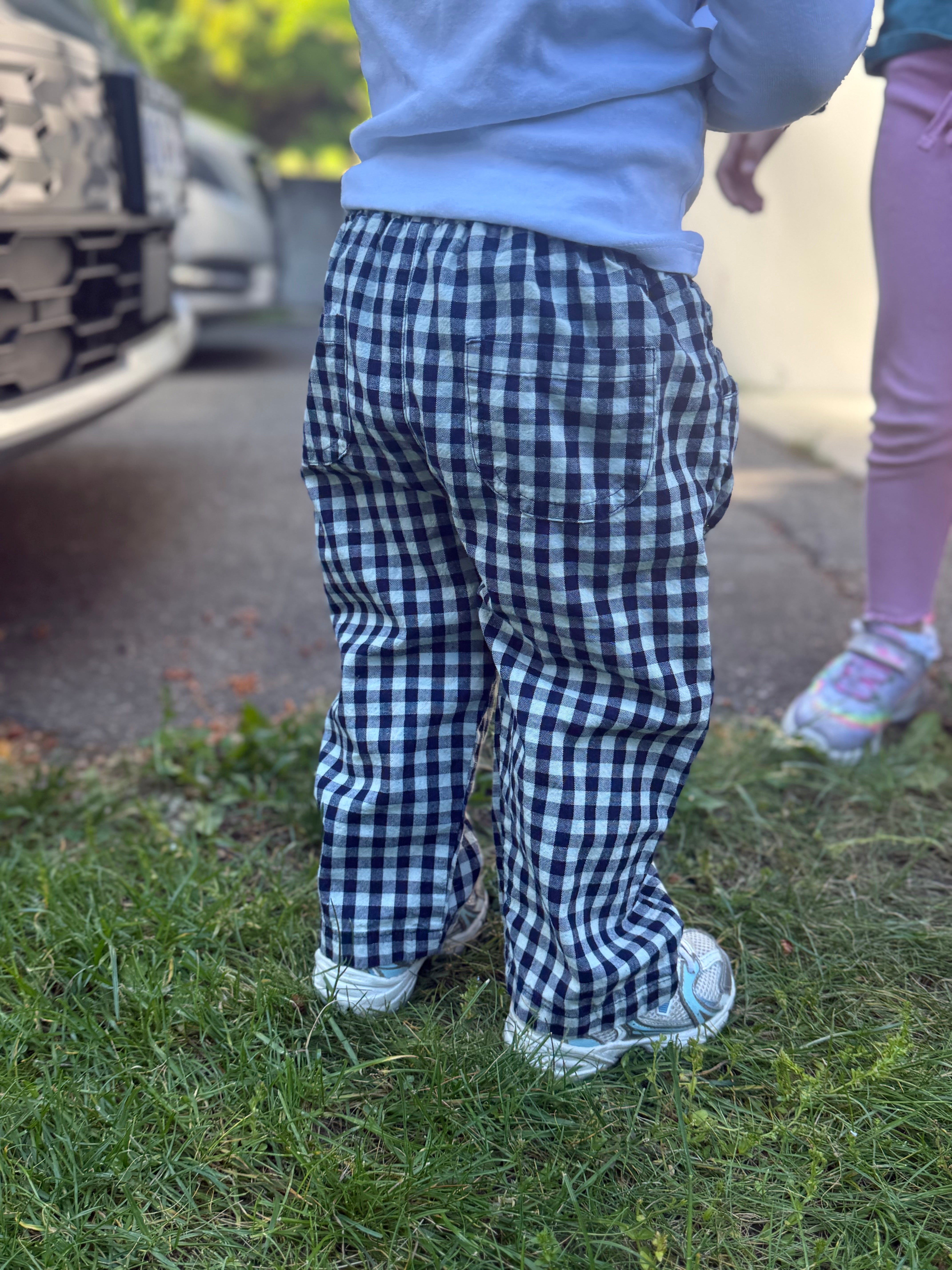 Child wearing blue checkered pants standing on grass with a blurred background