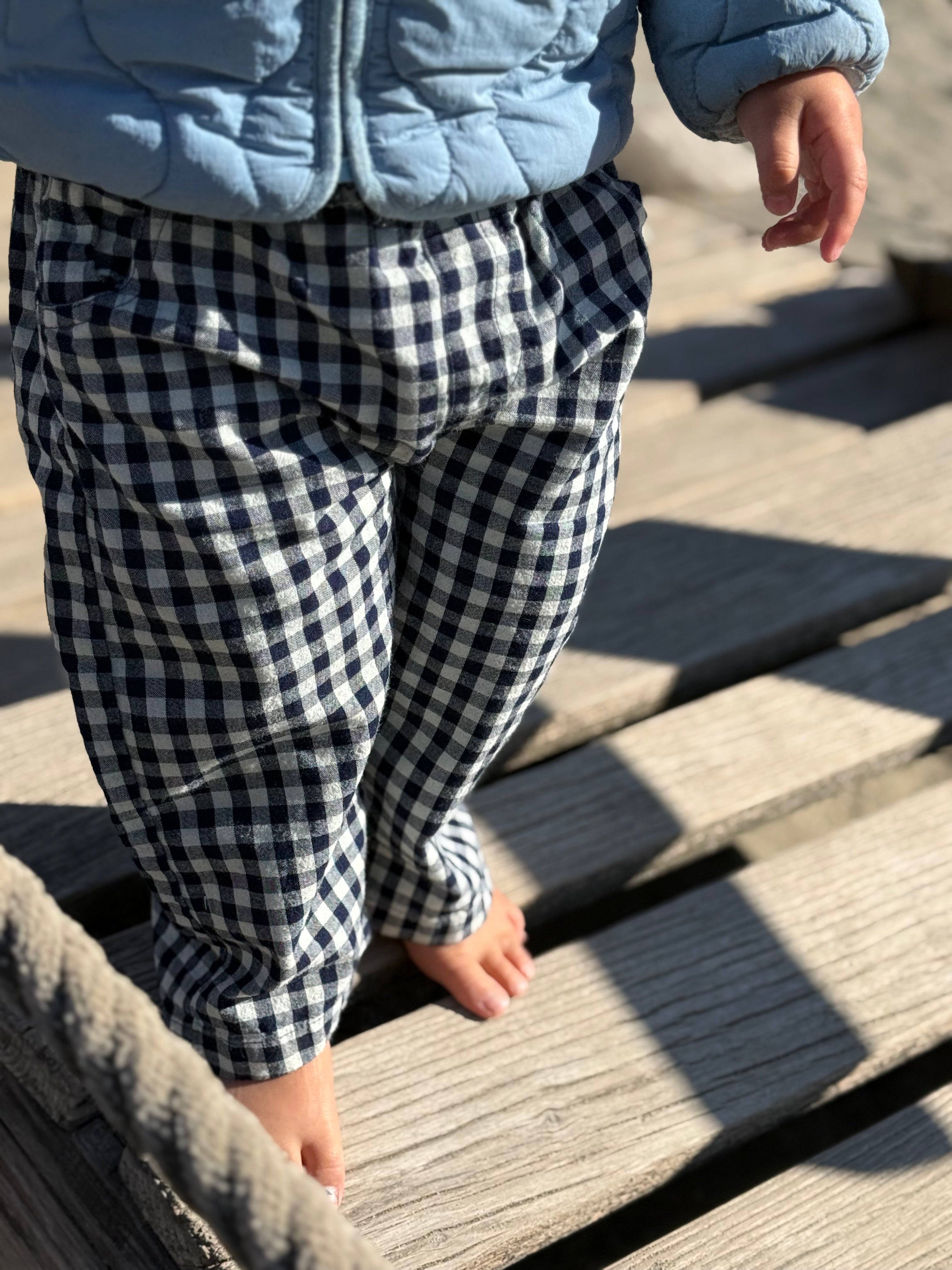 Child wearing a blue quilted jacket and black and white checkered pants walking on wooden steps.