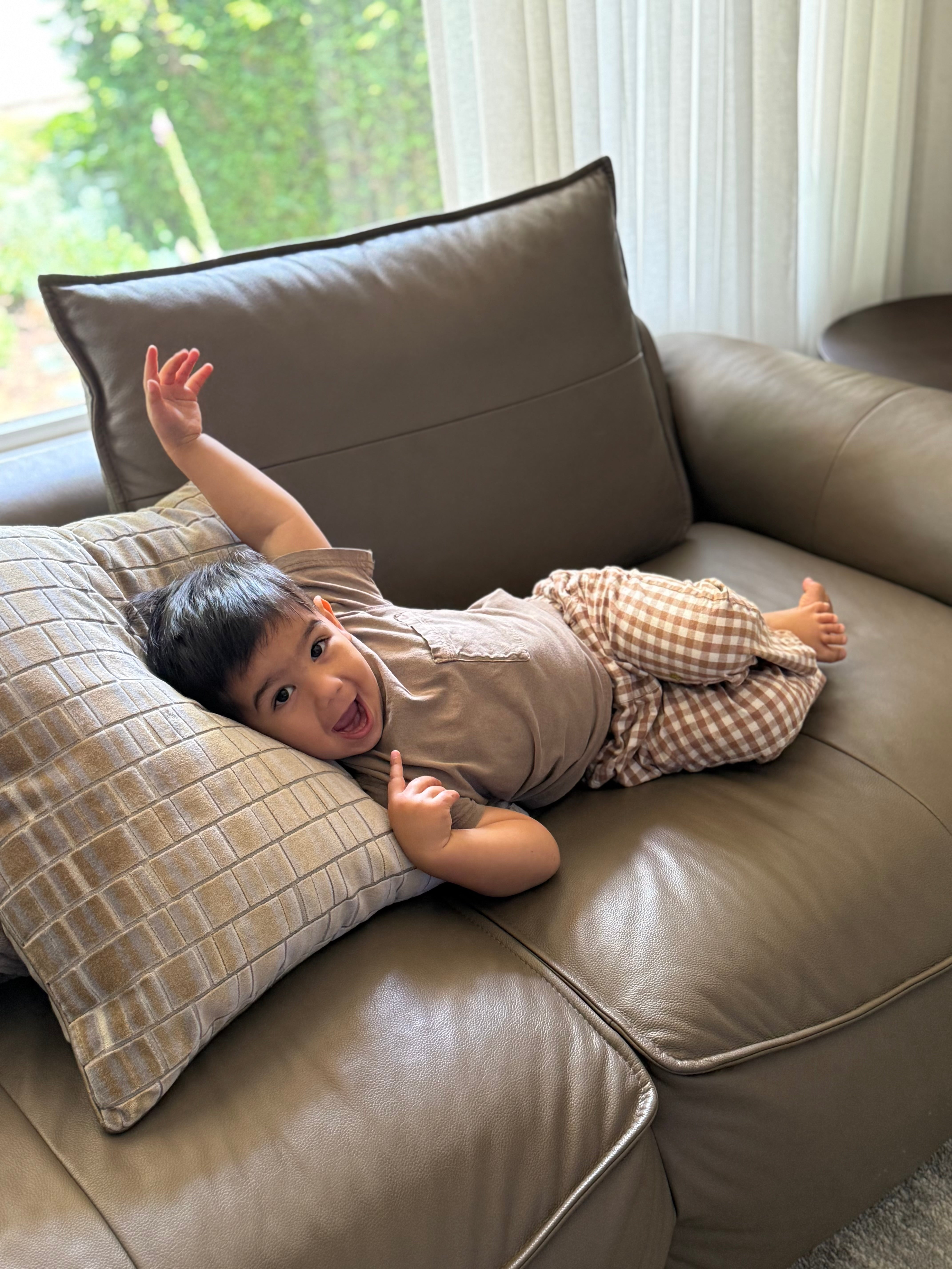 Child lying on a brown sofa with pillows in brown gingham trouser pants 