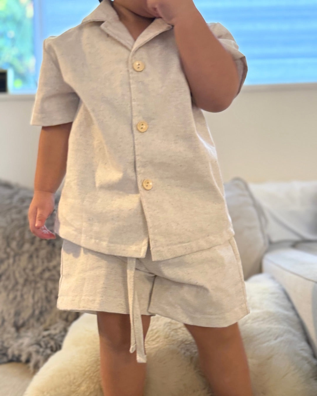 Child wearing a beige outfit with buttons in a home setting