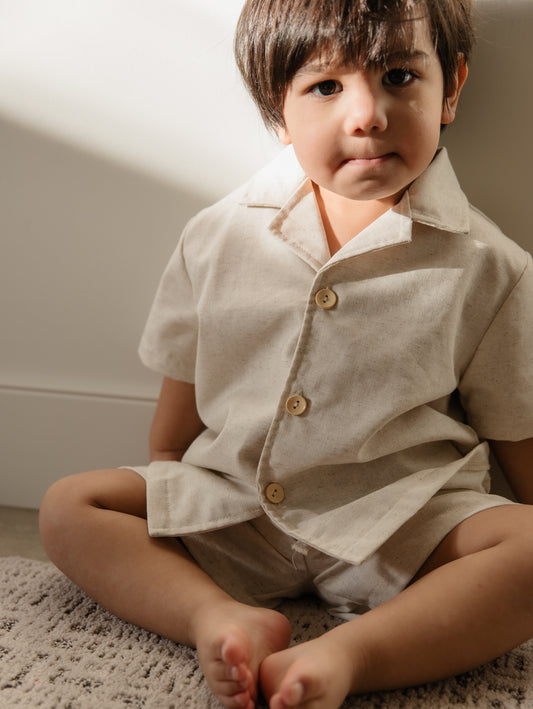 Child wearing a beige shirt with buttons sitting on a carpeted floor.
