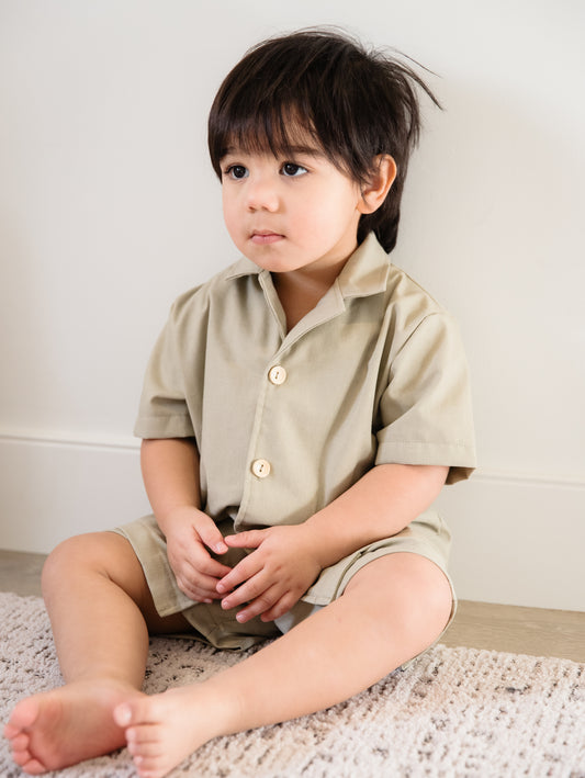 Child wearing a beige shirt and shorts sitting on a carpeted floor.