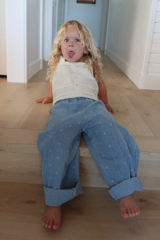 Toddler wearing jeans with stars and stripes while sitting on light wood steps, sticking her tongue out