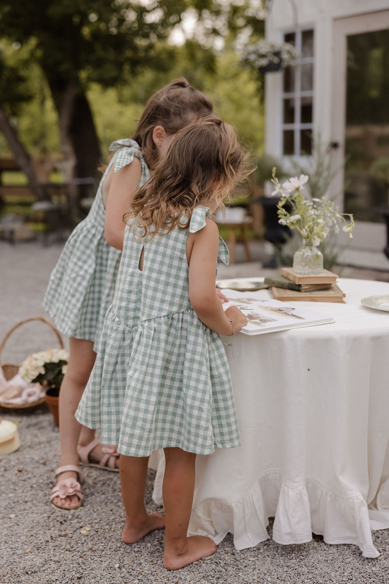 two toddler girls wearing beautiful twirly sage green and white gingham dresses with their backs to the camera